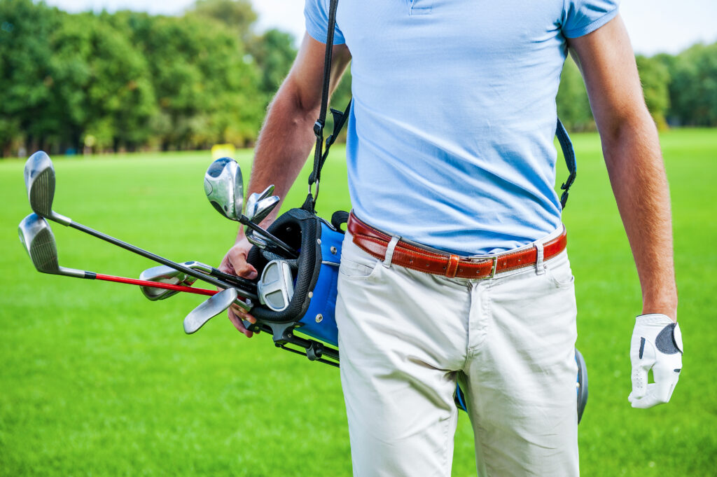 Close-up of male golfer carrying golf bag with drivers while walking by green grass
