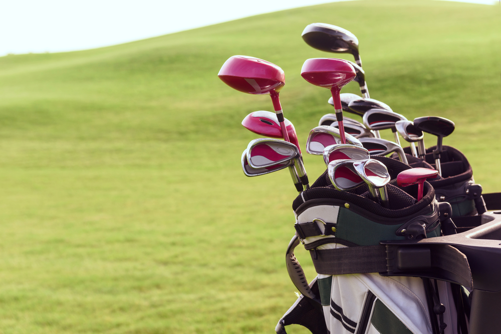 Close up of bag full of different golf clubs on background of green course.