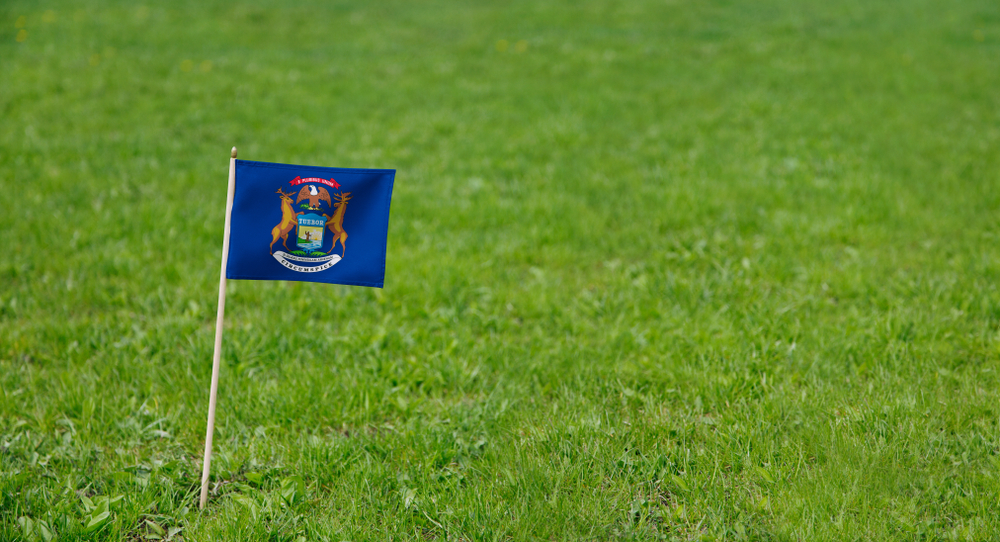Michigan flag. Photo of Michigan state flag on a green grass lawn background. Close up of state flag waving outdoors.