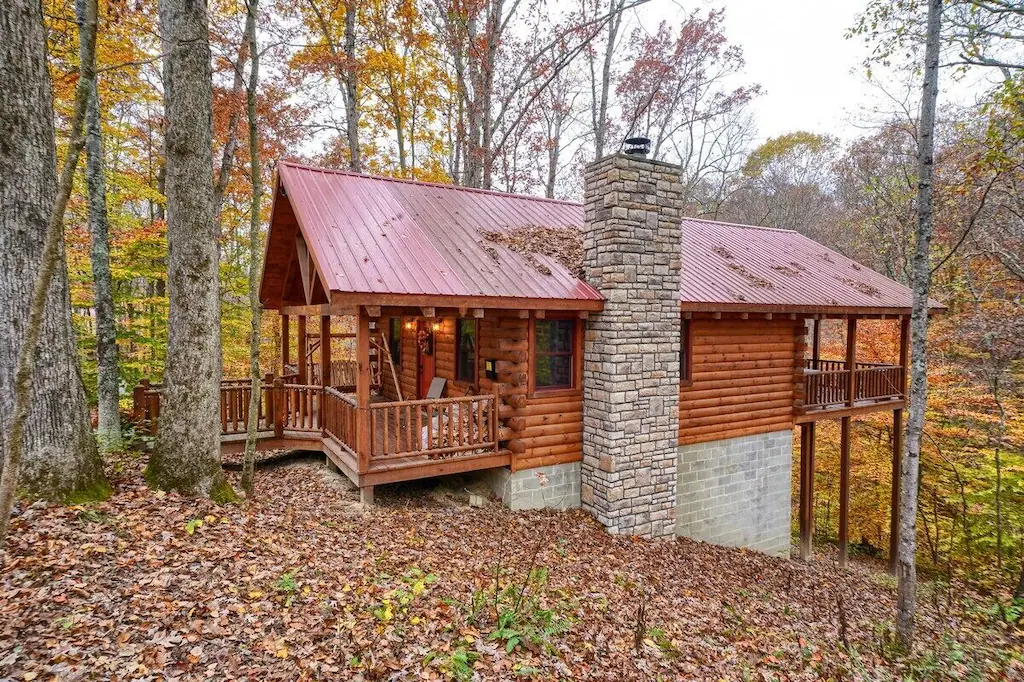Picture of a cabin with a stone fire place. The cabin has balconies that overlook woods. The article is about cabins with hot tubs.  