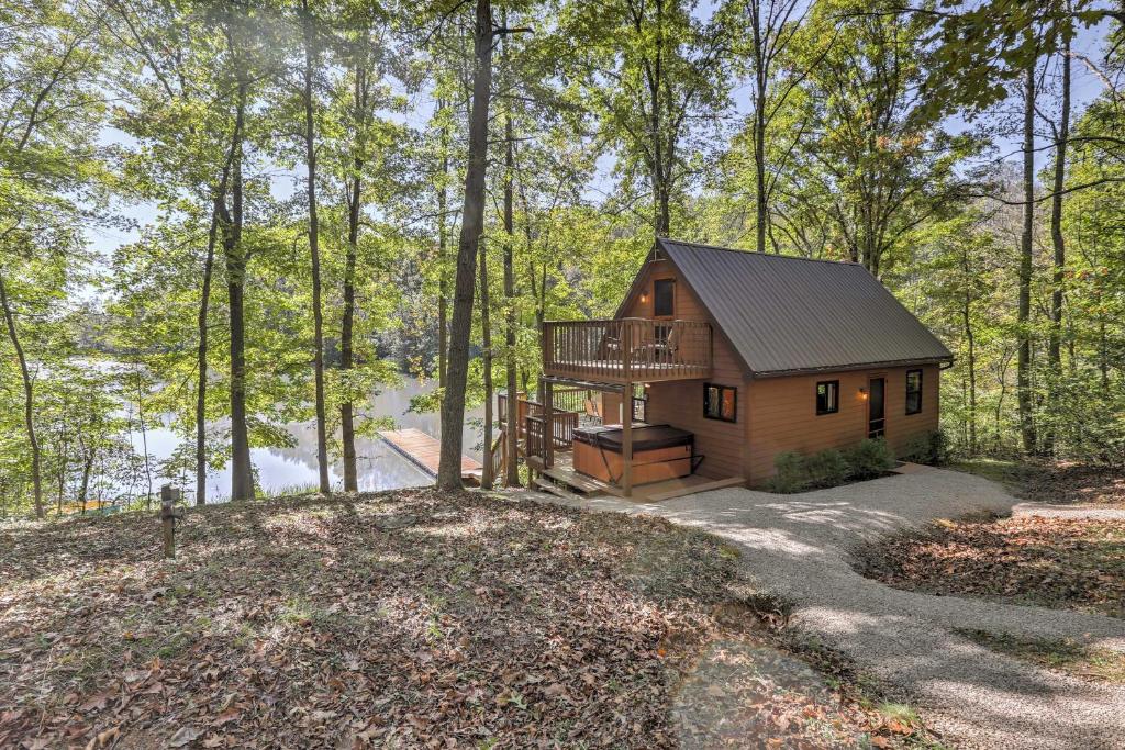 A cabin in the woods surround by trees. There is a hot tub and a deck leading out to the water. 