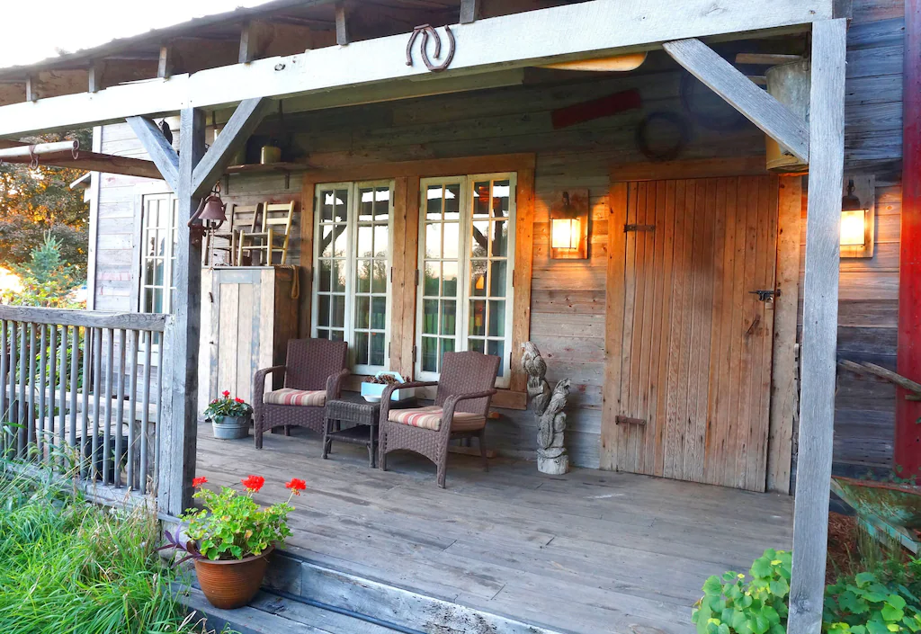 Porch of one of the cabins with hot tubs. There are two chairs on the porch in front of a large window.  