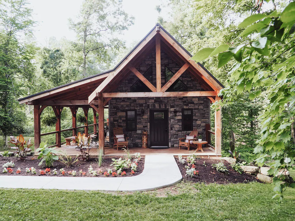 A beutiful cabin with a side porch and lovley garden. There are chairs outside th door. The article is about cabins with hot tubs. 