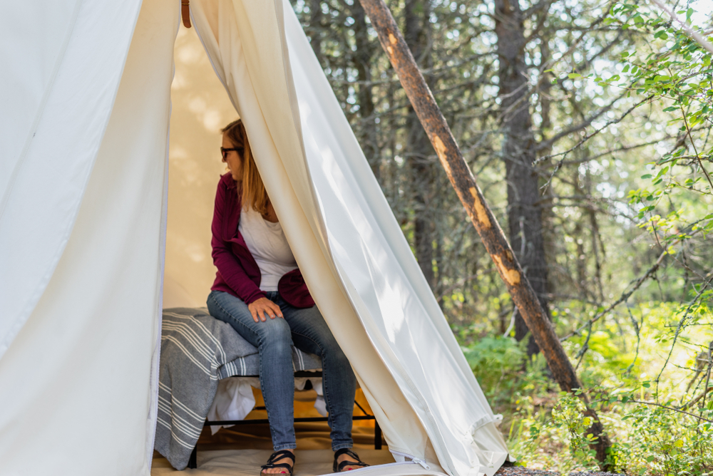 glamping trip - woman sitting on cot in canvas teepee. The article is about camping in Montana