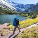 man walking with a daypack and a hiking stick on a trail with a lake and mountains hiking in montana