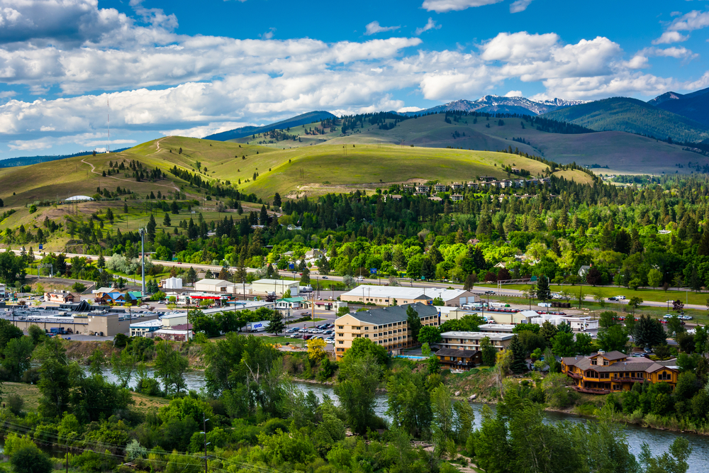 Looking down at the city of Missoula and the Fork Clark River with green, rolling mountains in the distance.