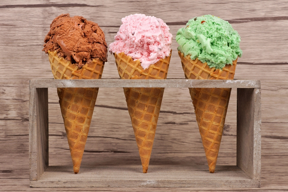 Three ice cream cones of different flavors sitting in a wooden display.