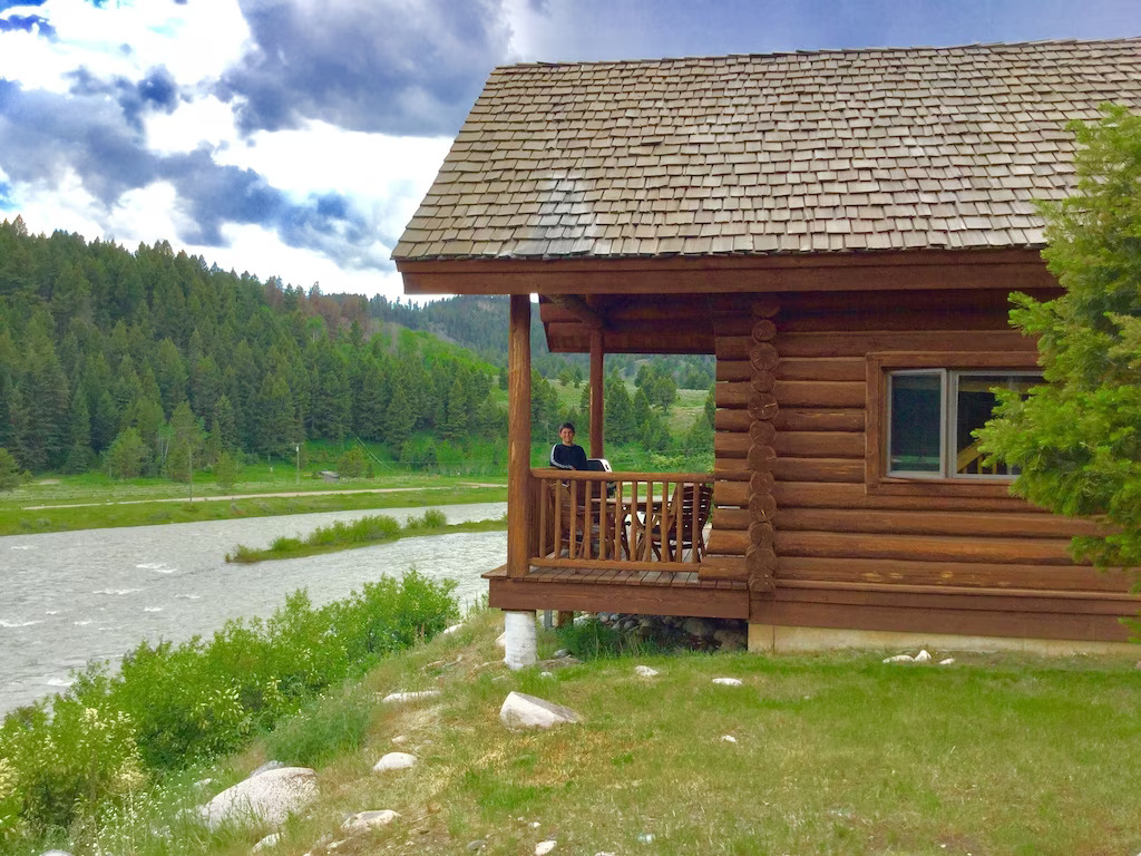 boy standing on the deck of a log cabin on a river cabins in montana