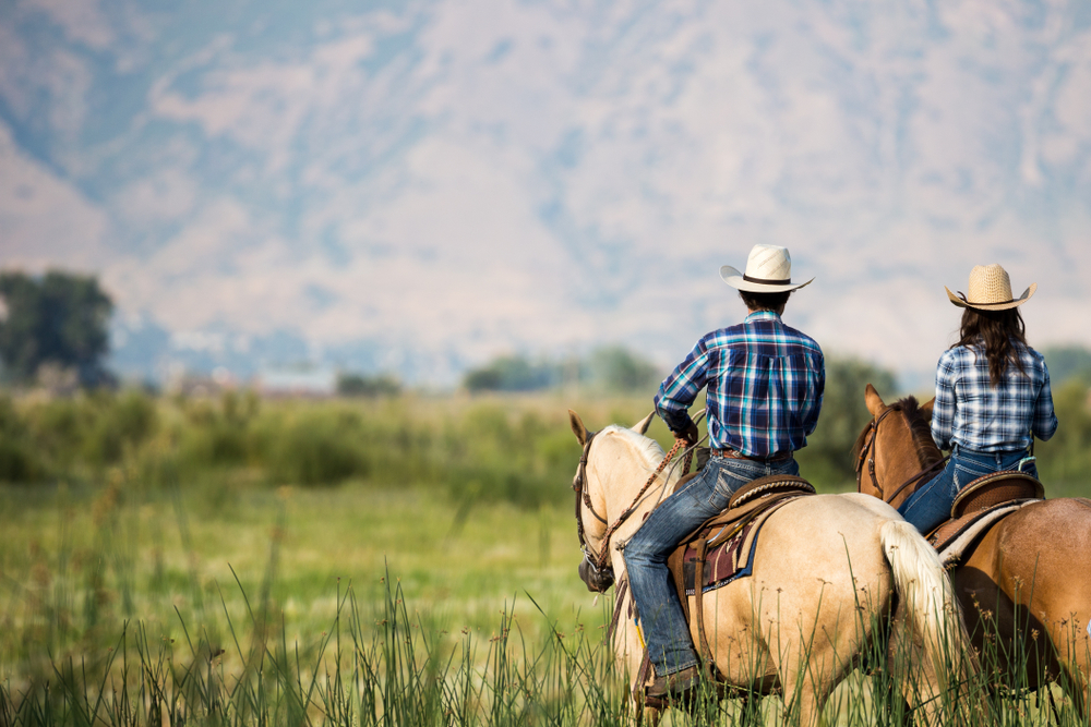 Couple in cowboy hats on horseback with a mountain in the distance.