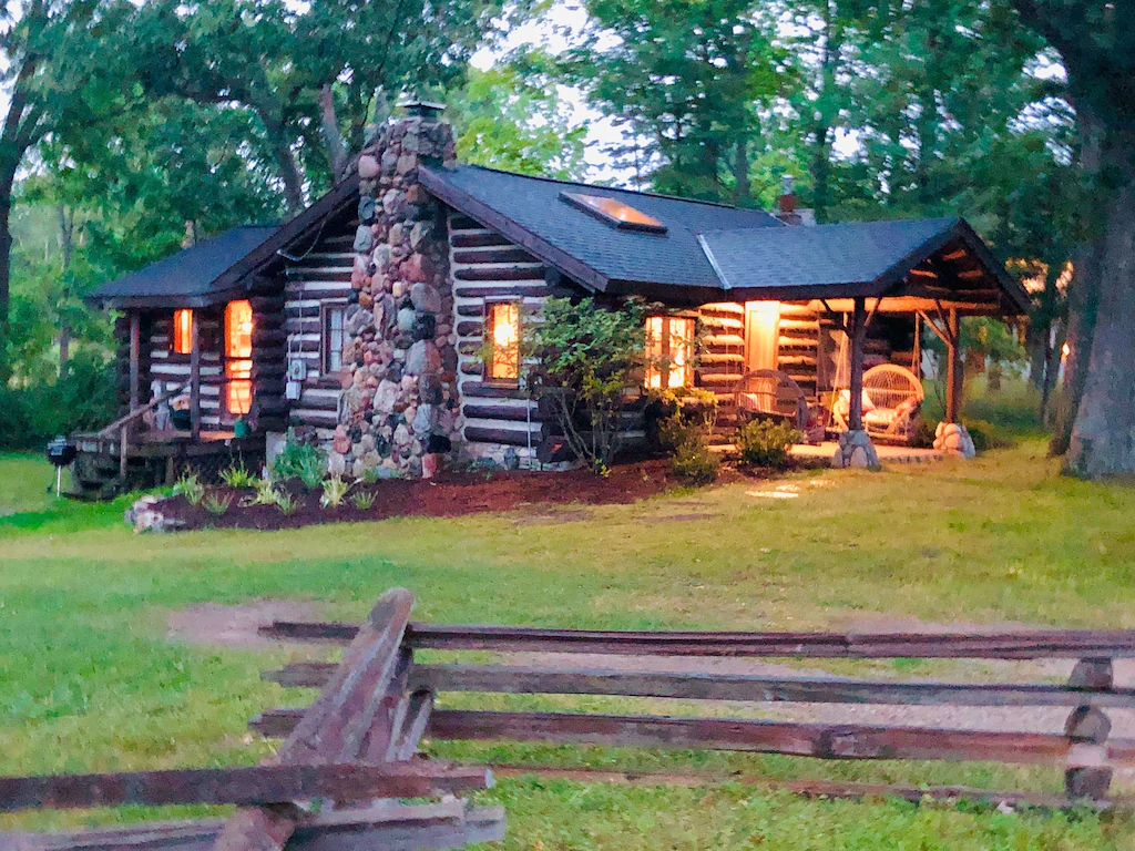 One of the cabins in Michigan. The cabin is in the woods and the picture is taken at night and there are lights on.  