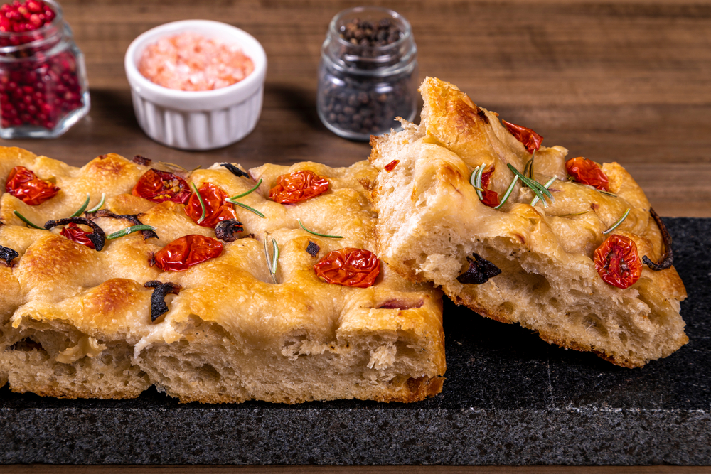 Homemade Italian Focaccia Modenese, with rosemary and olive oil on a rustic wooden background. The article is about restaurants in Helena 