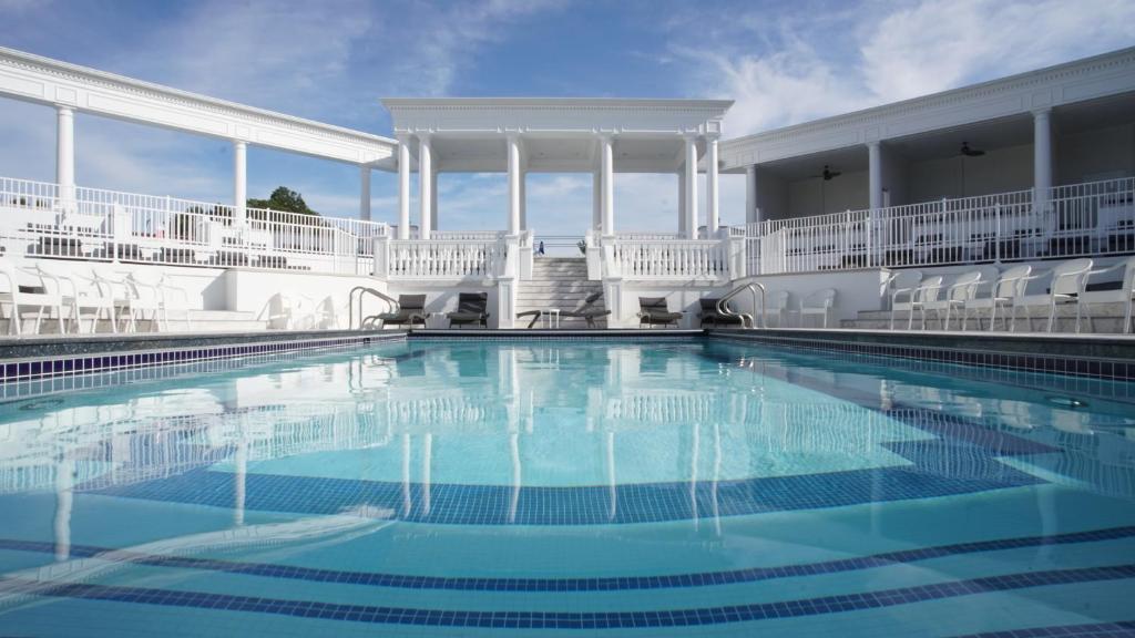 A pool with a white balcony around it and white chairs at the side. 