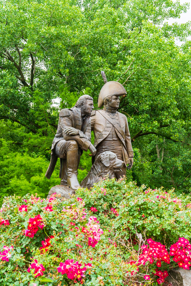 Lewis and Clark with a dog stature surrounded by flowers.