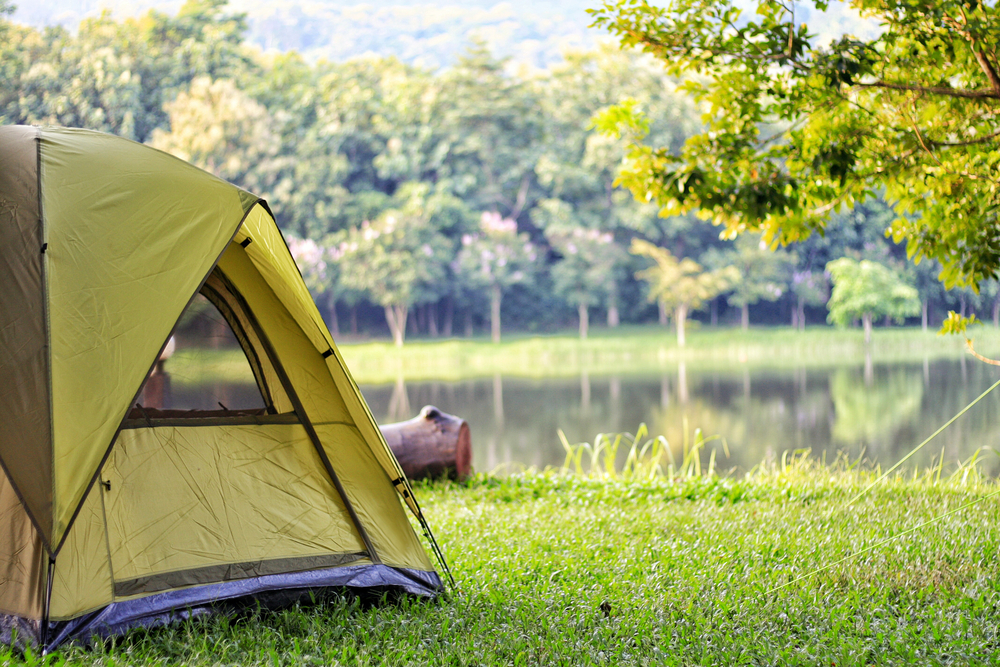 A tent pitched next to a lake a green trees in the Midwest.