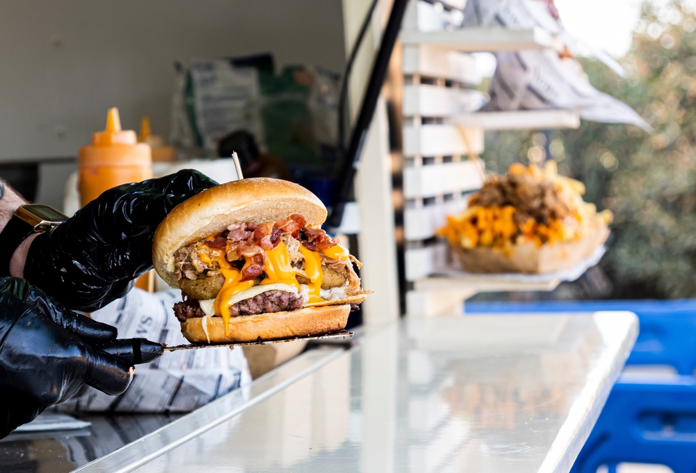  A food truck vendor wearing black cooking gloves showing off a stuffed cheeseburger