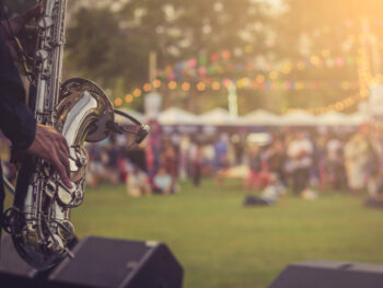 A closeup of a saxophone player with a field and crowd blurry in the background events in Michigan