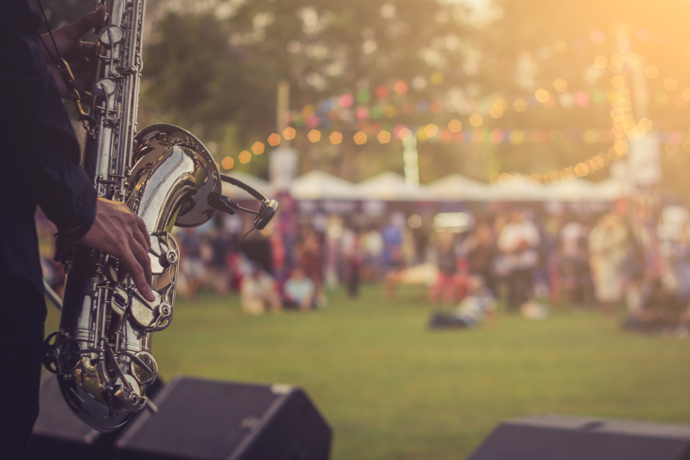 A closeup of a saxophone player with a field and crowd blurry in the background events in Michigan