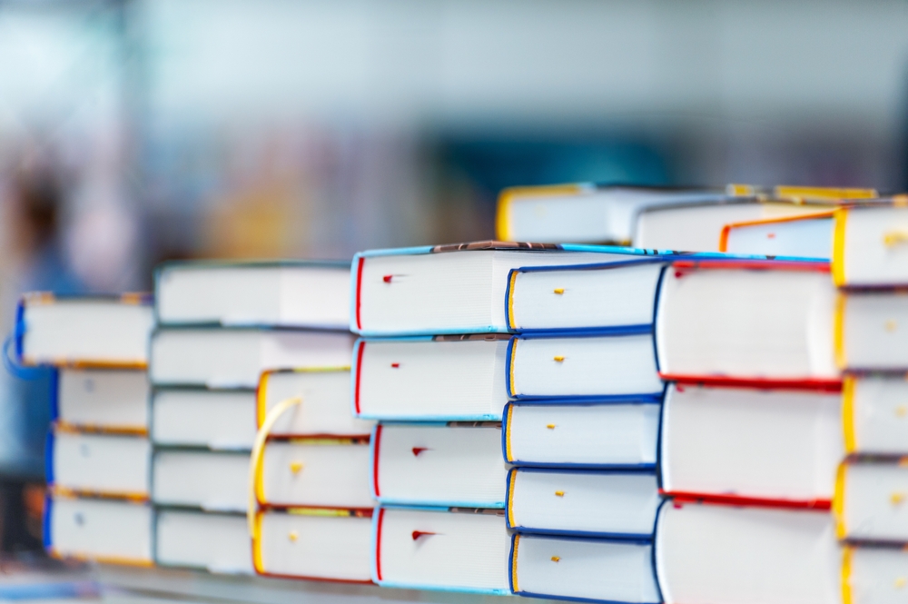 Stack of new books on the table. They have blue, red and yellow covers. 