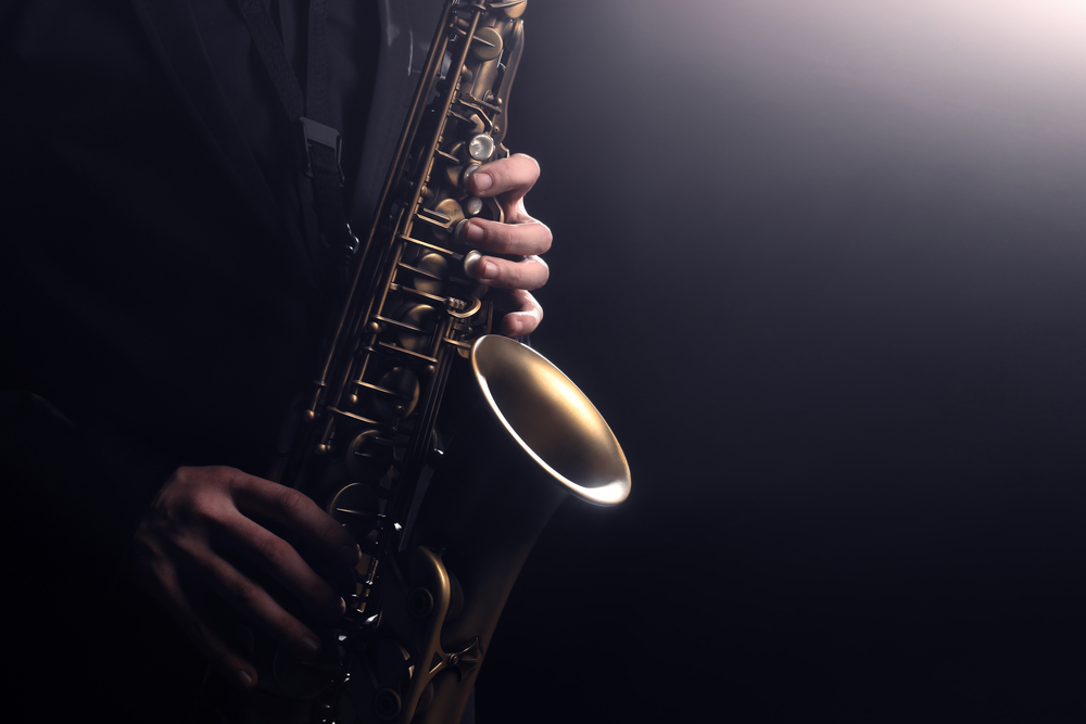 Saxophonist playing jazz music with a dark black background, the shot is close up. 