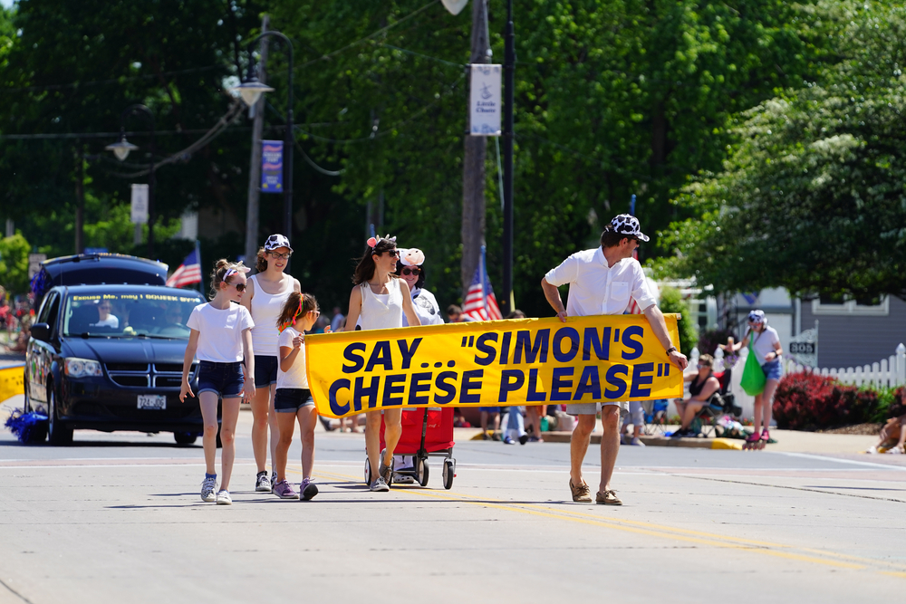 Local community members walking and participating in Great Wisconsin Cheese festival parade. They are holding a larges red and yellow banner.  