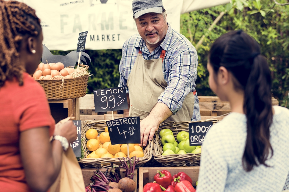 A man at a farmer's market produce stand talking to women customers