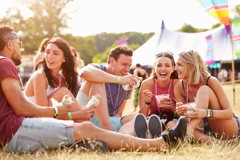 A group of young people sitting on the grass and eating something at an outdoor events in Michigan