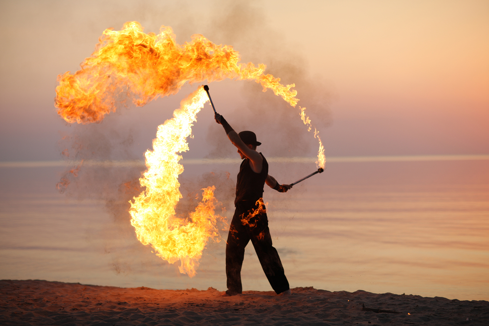A fire performer using fire batons on a a beach