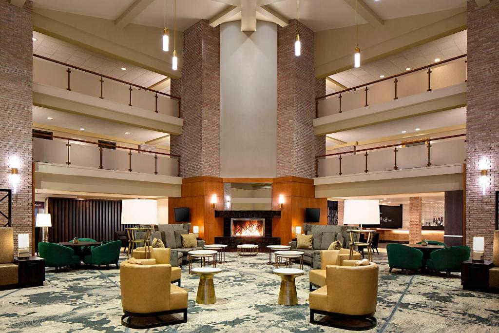 A hotel lobby with green and gold chairs and a large fireplaces. Rooms and corridors look out over the atrium.  