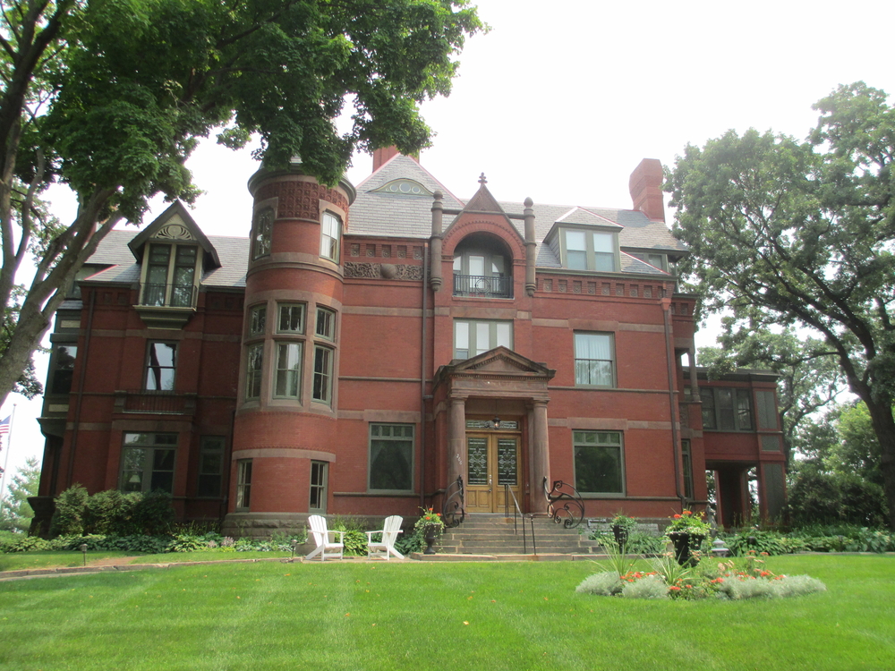 The exterior of a brick historic home with trees and a large green lawn