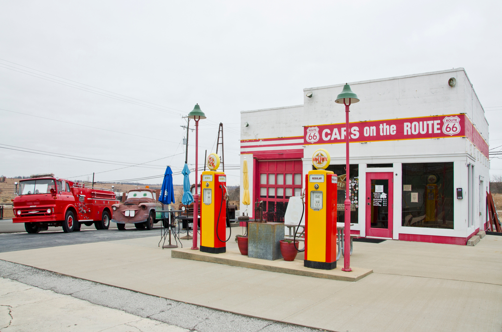 Small, red and white painted service station with retro gas pumps out front and a fire truck and tow trucks on the side.