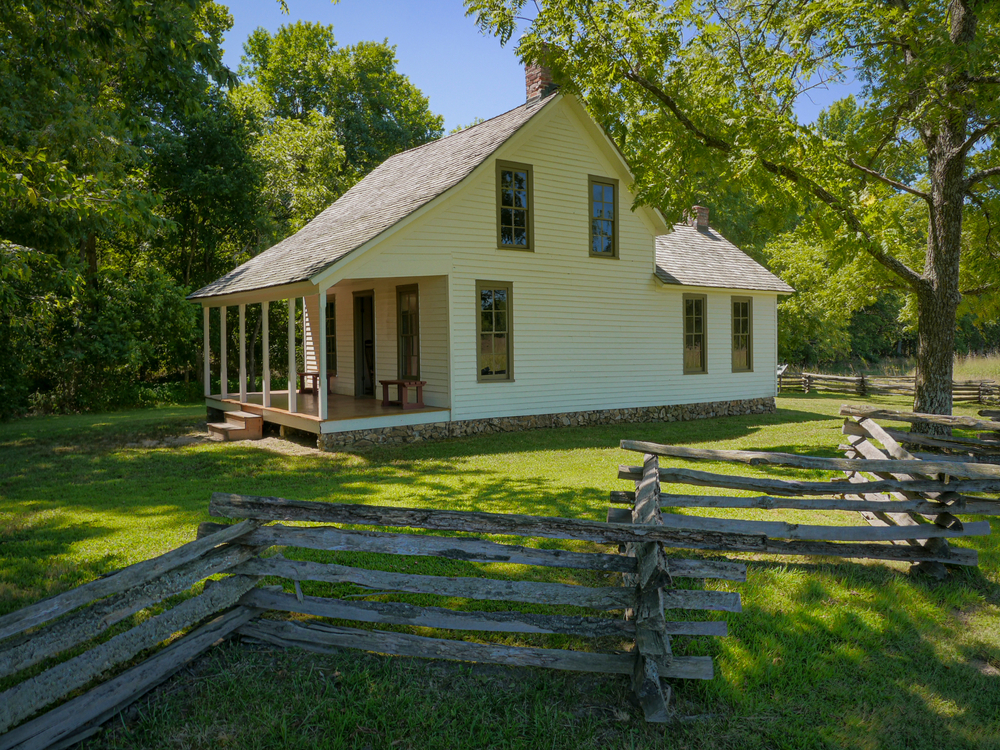 Small white, wooden house with a log fence around it next to many trees at the George Washington Carver National Monument.