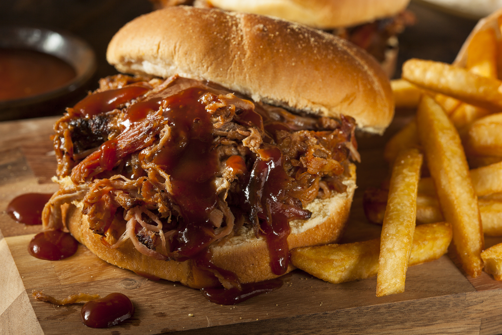 Close up of a pulled pork sandwich with BBQ sauce on it and fries on the side.