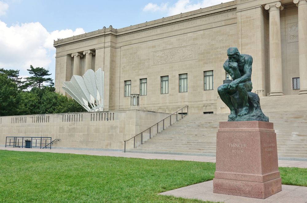 The Thinker statue outside of the Nelson-Atkins Museum of Art with one of the shuttlecock sculptures in the background.