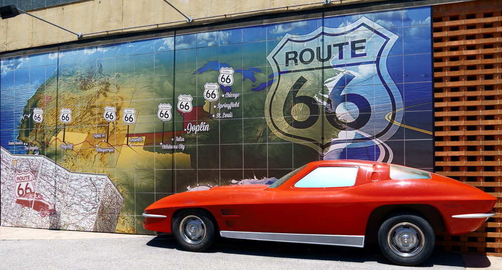 A fake red Corvette in front of a mural of a Route 66 map.