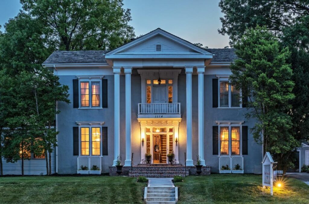 Dusk over a historic two-story columned home with lit up windows.