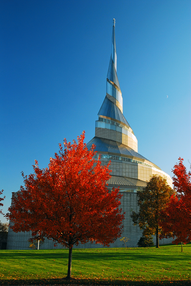 The stainless steel spiral steeple of the Community of Christ Temple with fall trees on a sunny day.