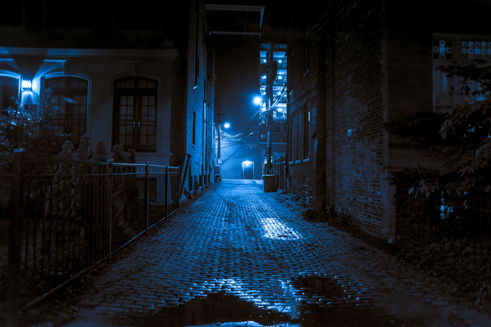 A dark alley in a town with a blue light shinning in it