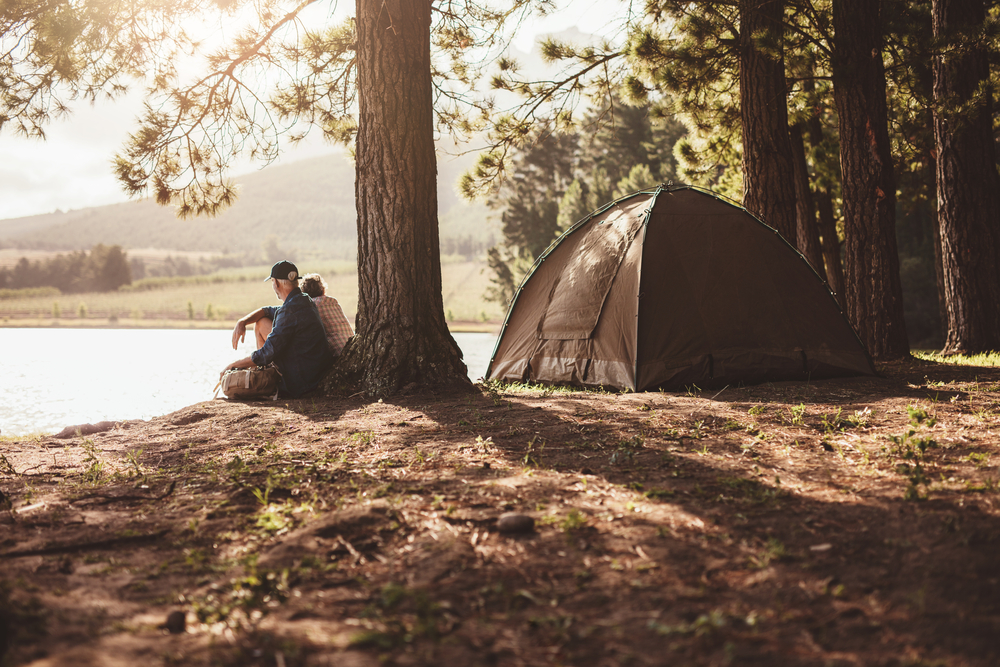 A senior couple sitting next to a lake with a tent behind them on a sunny day