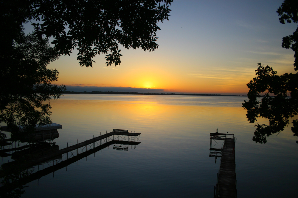 The sun setting over a quiet lake in Iowa with small docks and surrounded by trees