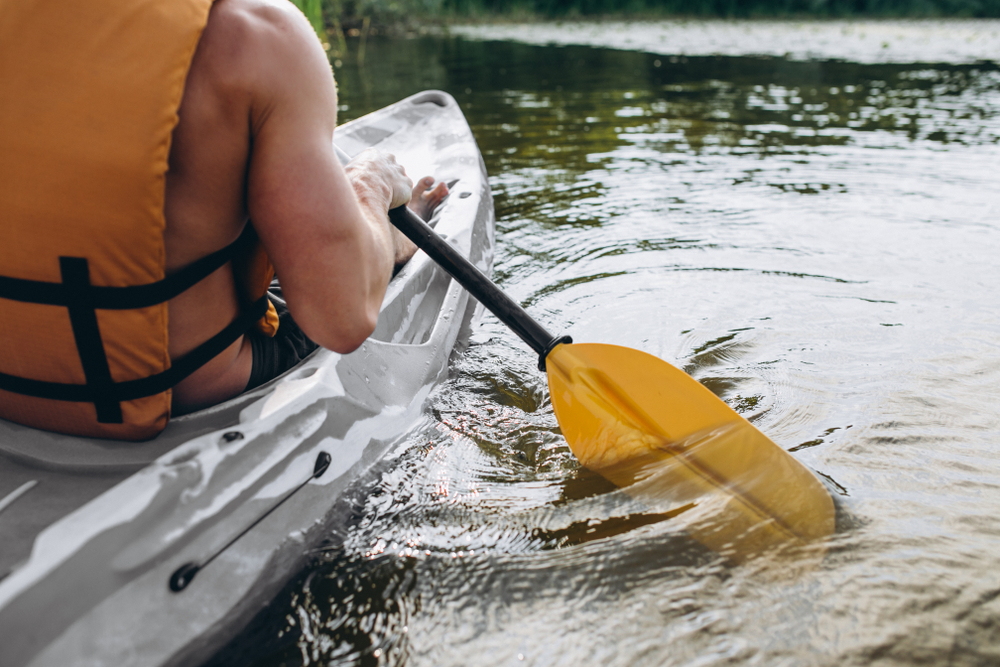 Young man kayaking on the river the picture is close up and you can see the oar and part of the boat. 