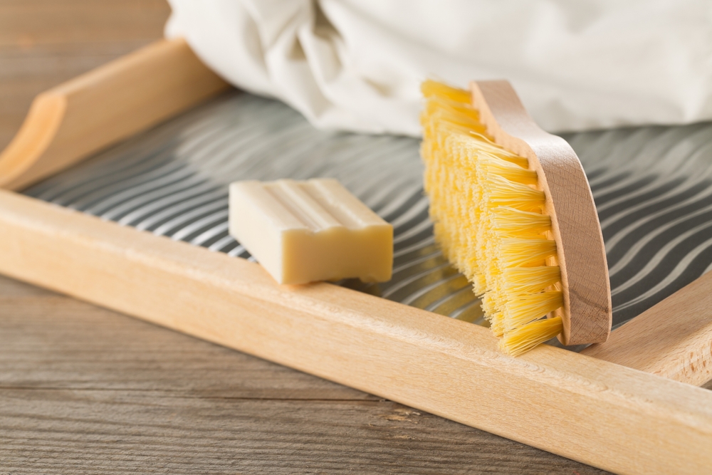 Close up of wood and metal washboard or wash board with brush, piece of washing soap and white shirt on wooden background, selective focus