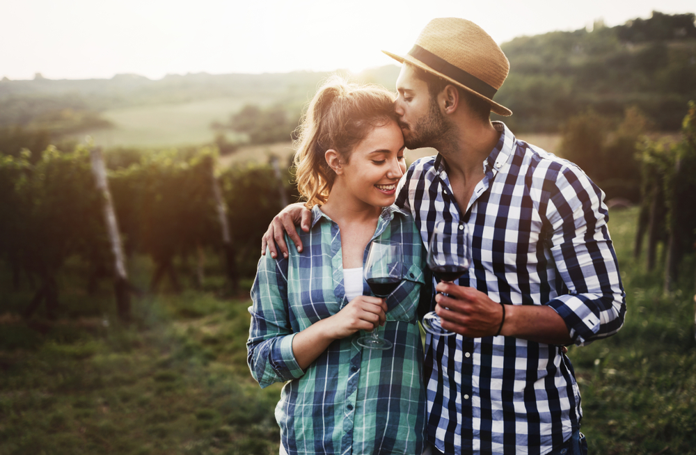 A couple hugging each other with glasses of wine in a vineyard