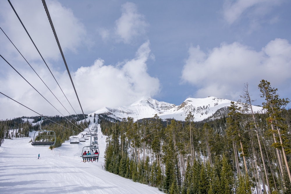View from a ski lift of trees and snowy mountains.