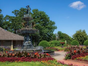 Tiered fountain with a statue on top surrounded by colorful flower beds in Clemens Gardens, one of the best things to do in St. Cloud, MN.