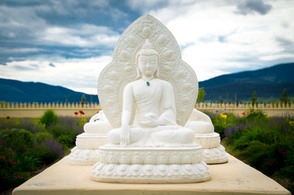 Close up of one of the white Buddha statues with gardens and mountains in the background.
