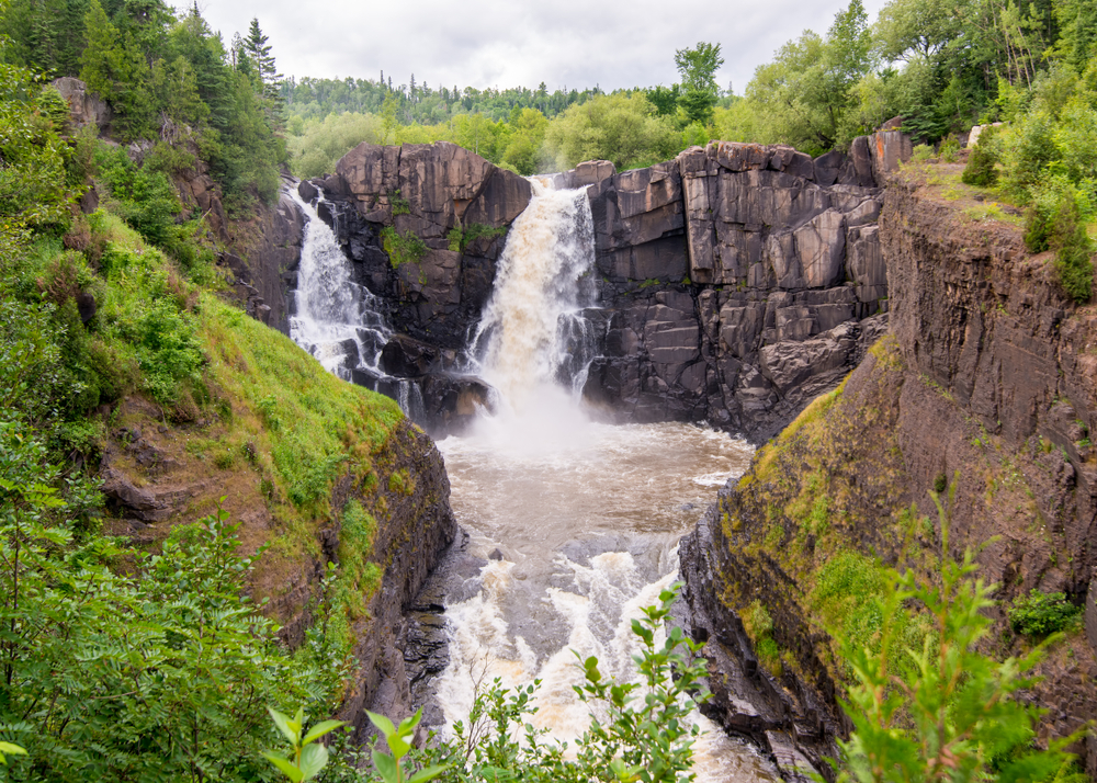 Two cascades of High Falls flowing over a rocky cliff into a gorge in Grand Portage State Park, one of the best attractions in Minnesota.