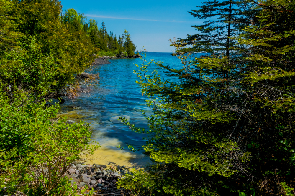 View through green trees of the blue water around Isle Royale National Park.