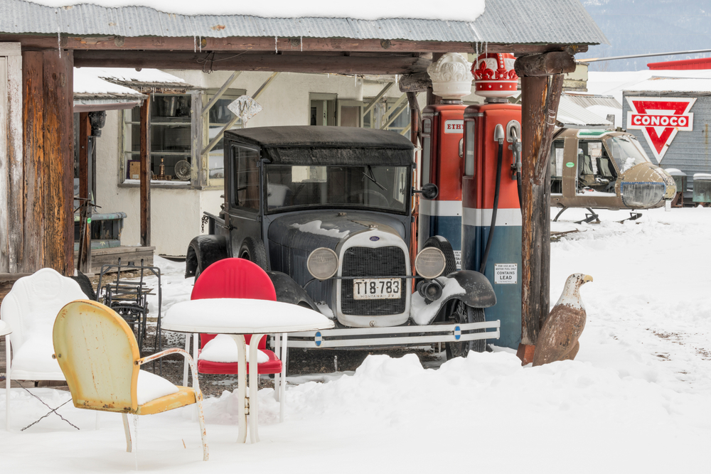 Antique car next to retro gas pumps on a snowy day with a helicopter in the background.