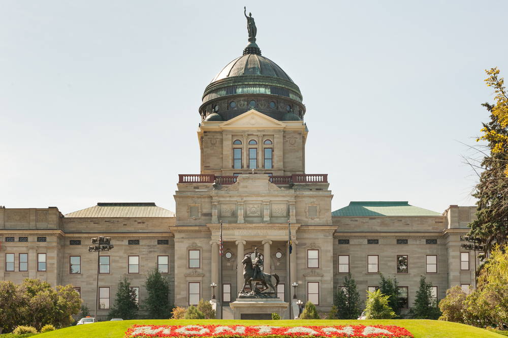 The Montana State Capitol building with a statue on its dome overlooking a statue on horseback and a flower bed spelling out the word Montana.