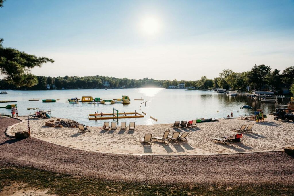 Lake beach with many chairs on the sand and a floating obstacle course in the water.